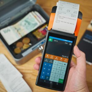 Photo by Hook Tell Close-up of a handheld payment terminal printing a receipt, with cash and coins visible.