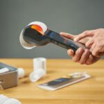 Hands operating a portable receipt printer with printed receipts on a wooden table.